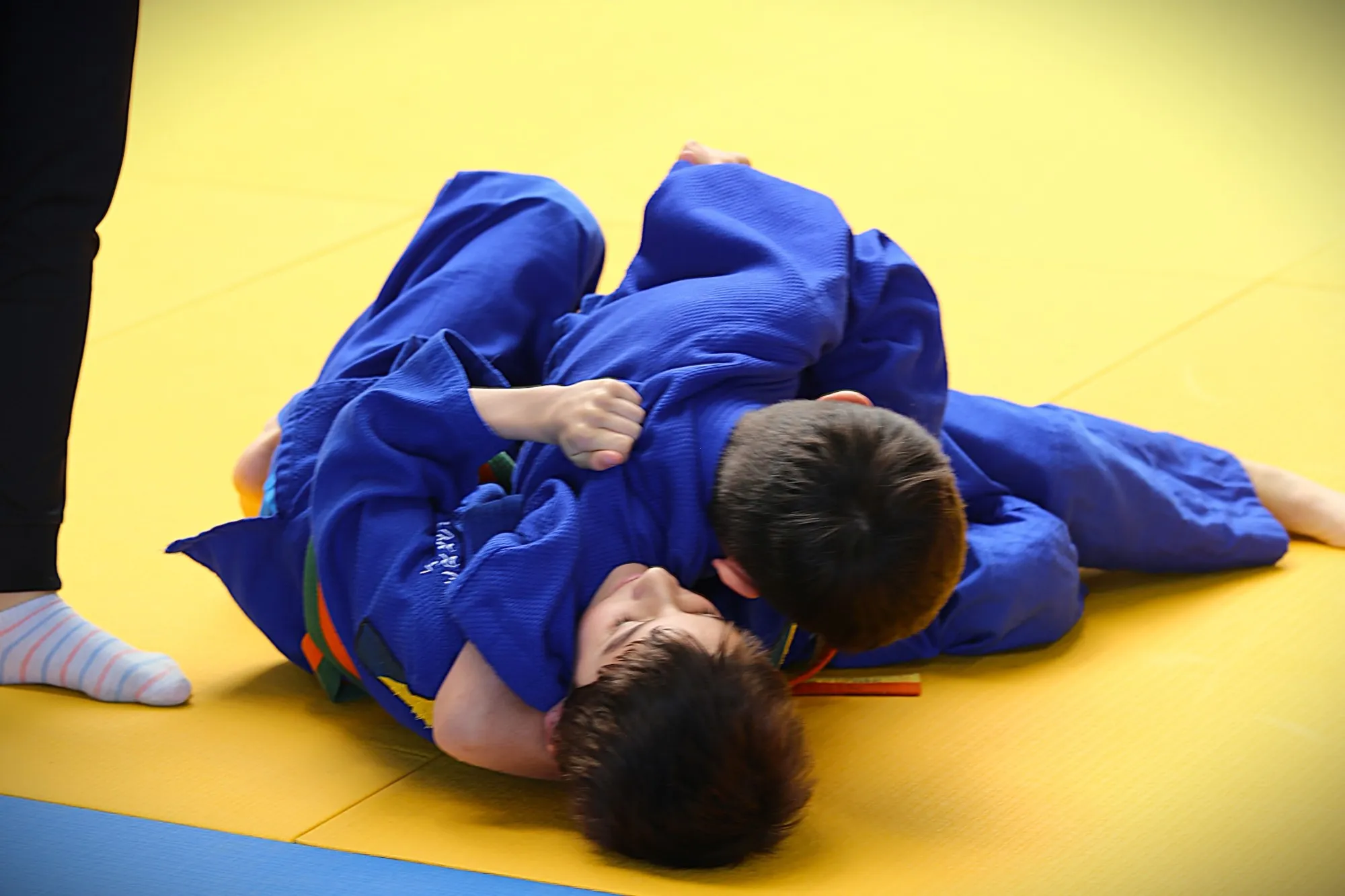 Dos judokas con judogi azul trabajan una inmovilización en el suelo